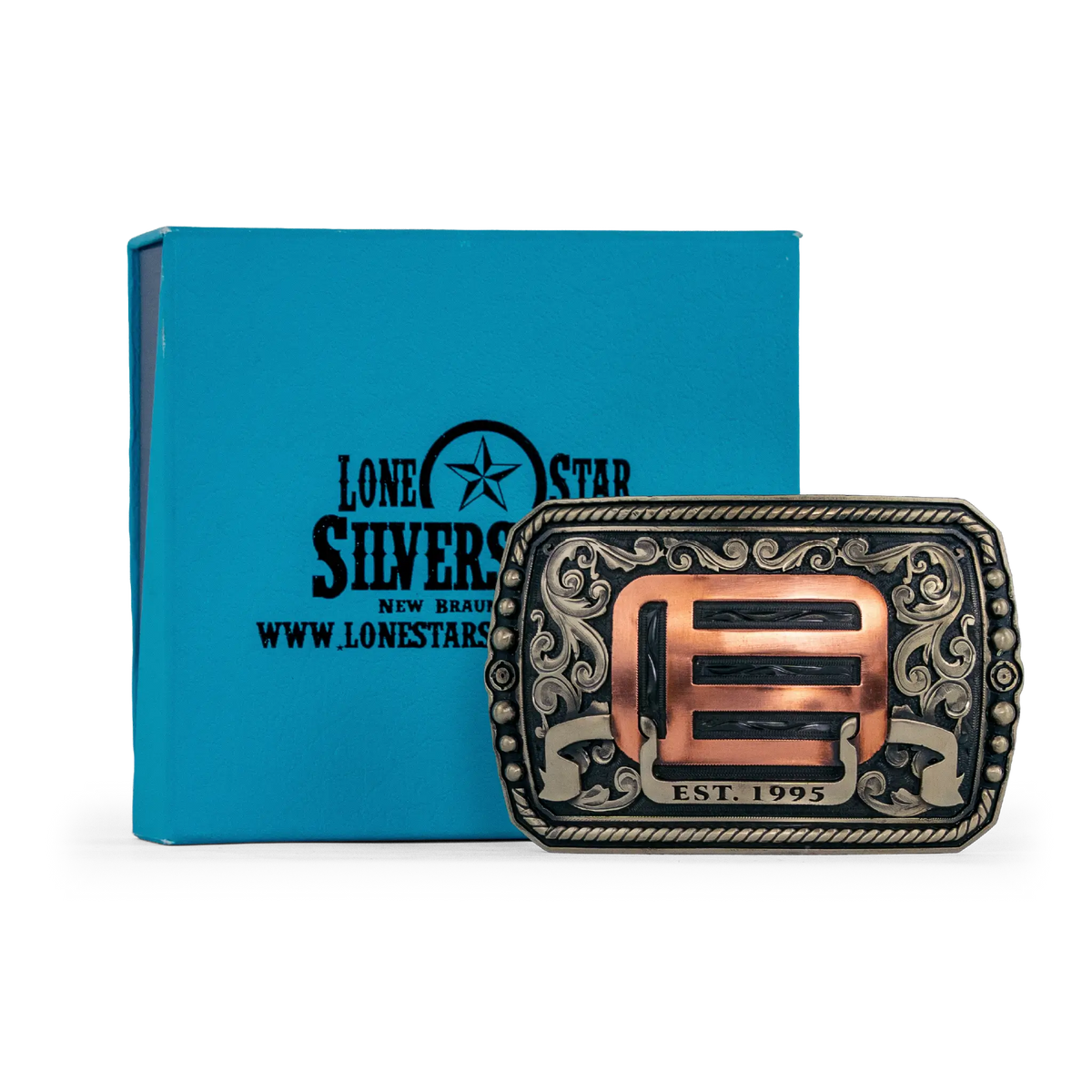 An ornate western-style belt buckle with gold-toned metal edges, and copper-toned scrollwork and geometric details, shown alongside its box on a white background.