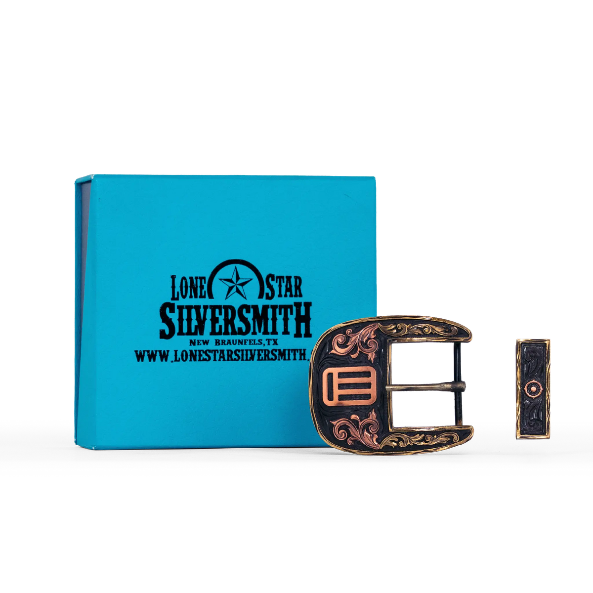 A decorative silver smith buckle with ornate filigree detailing, shown next to its turquoise branded presentation box on a white background.