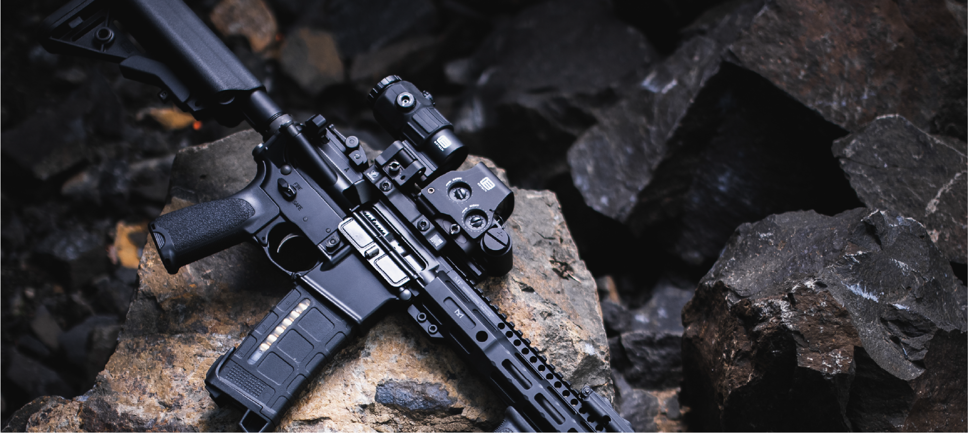 Black rifle with EOTECH HWS optic and magnifier on a rocky surface
