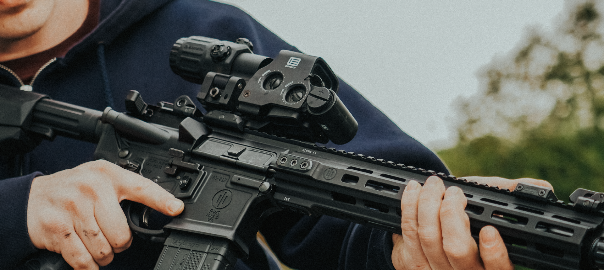 Person holding a rifle with black EOTECH HWS optic and magnifier outdoors
