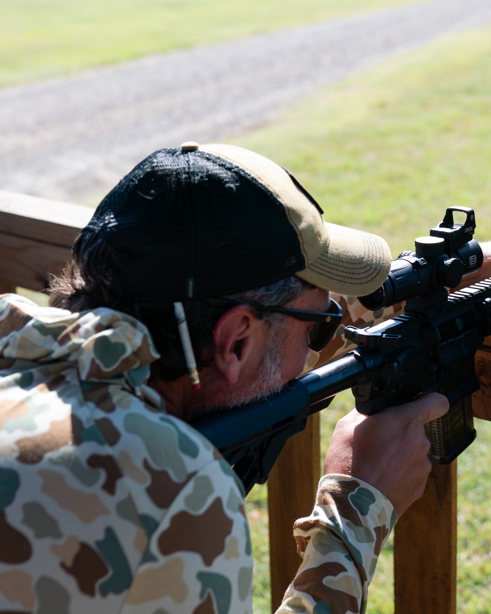 Person in camouflage Free Fly hoodie and hat shooting on a wooden structure with a clear blue sky.