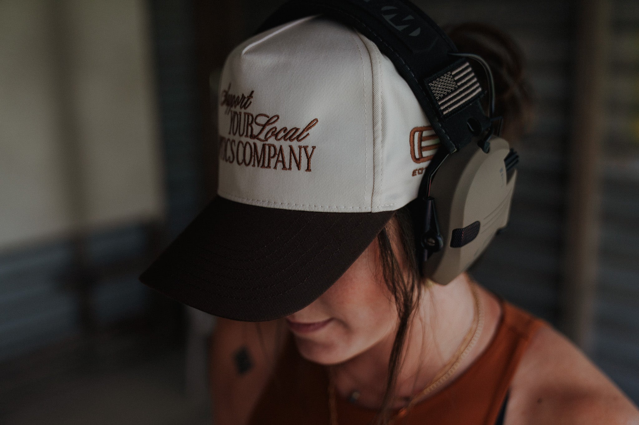Female wearing a cap with 'support your local optics company' and an EOTECH logo, blurred background