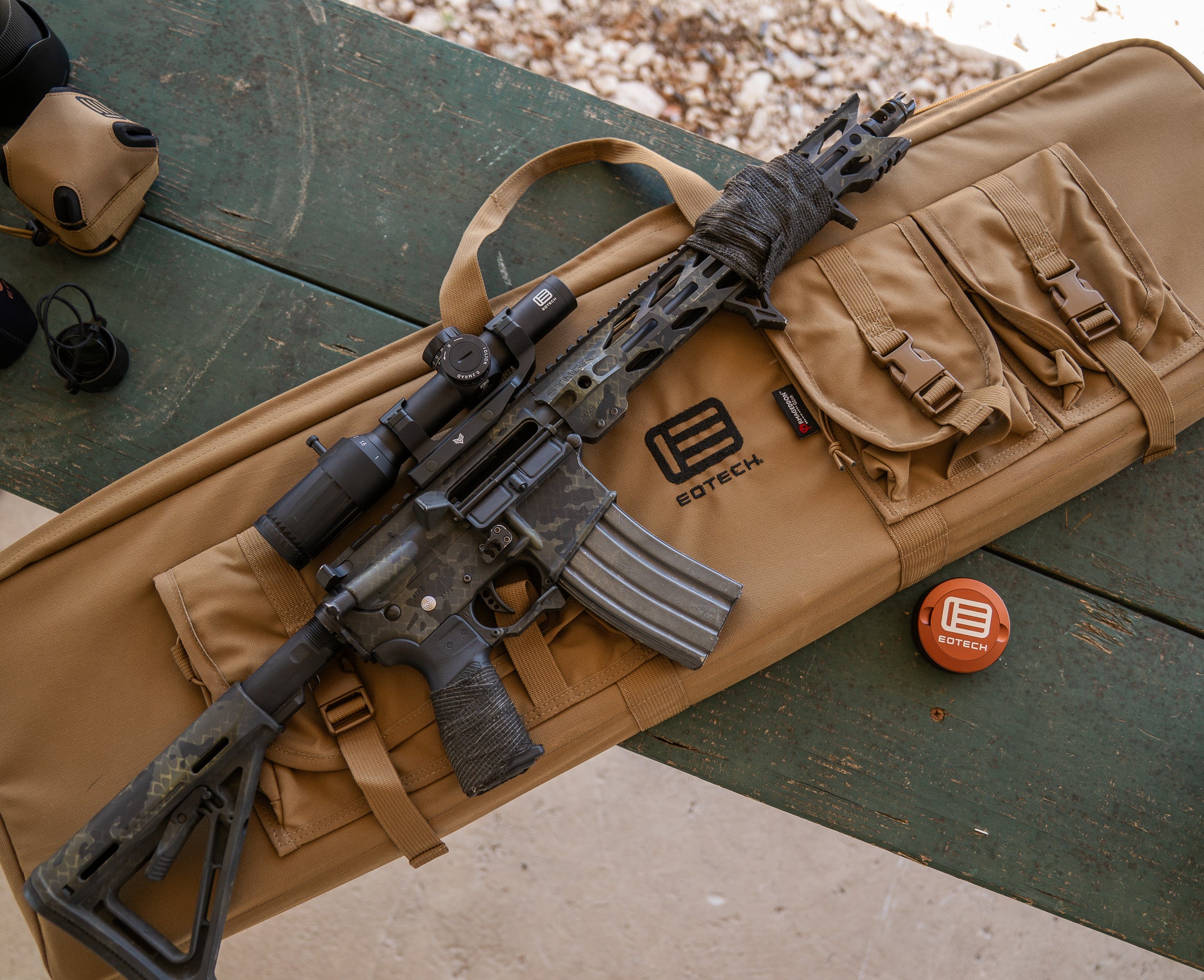 Rifle on a brown carrying case with EOTECH logo and Vudu scope on a green surface