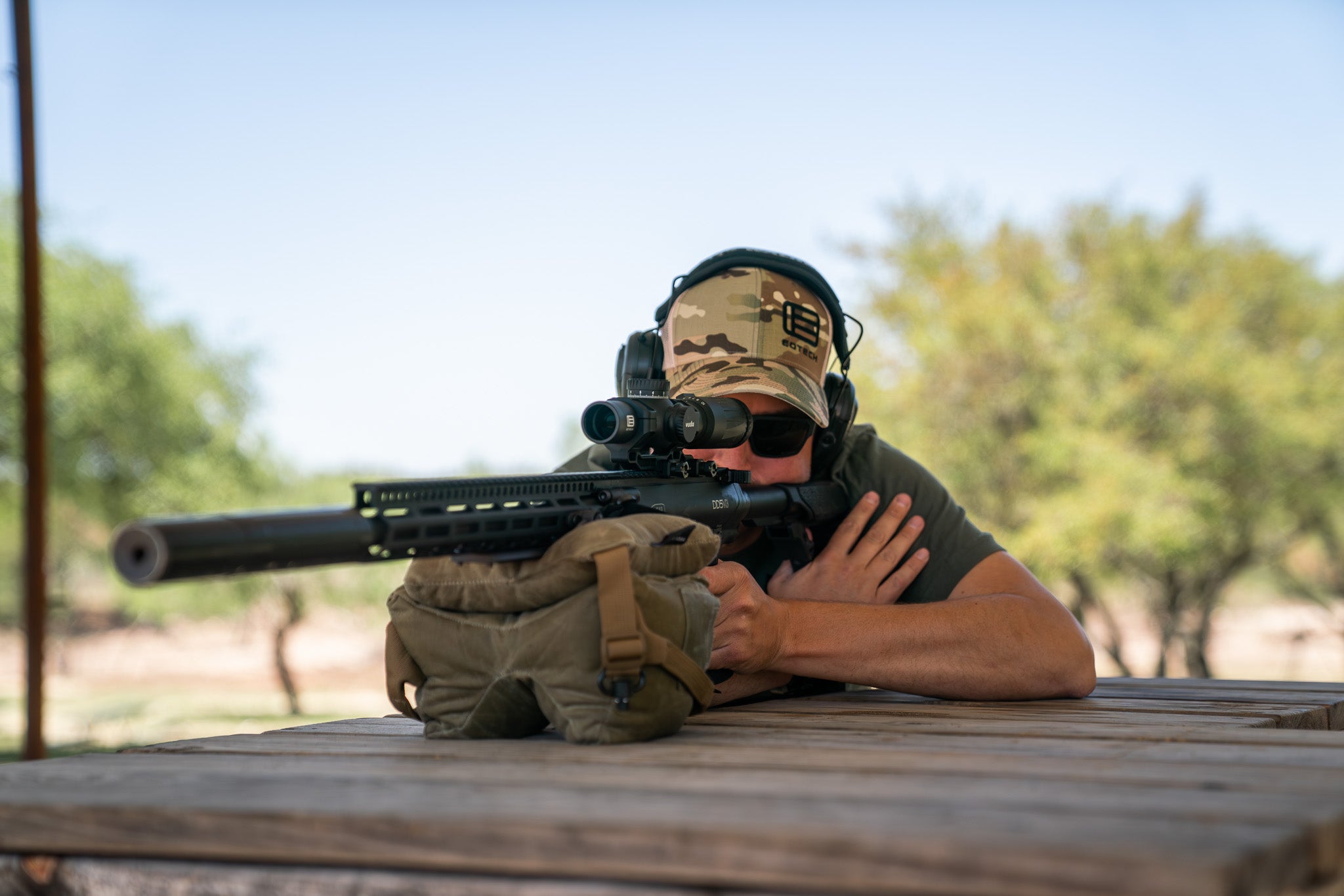 Man at bench rest with black rifle and EOTECH Vudu scope