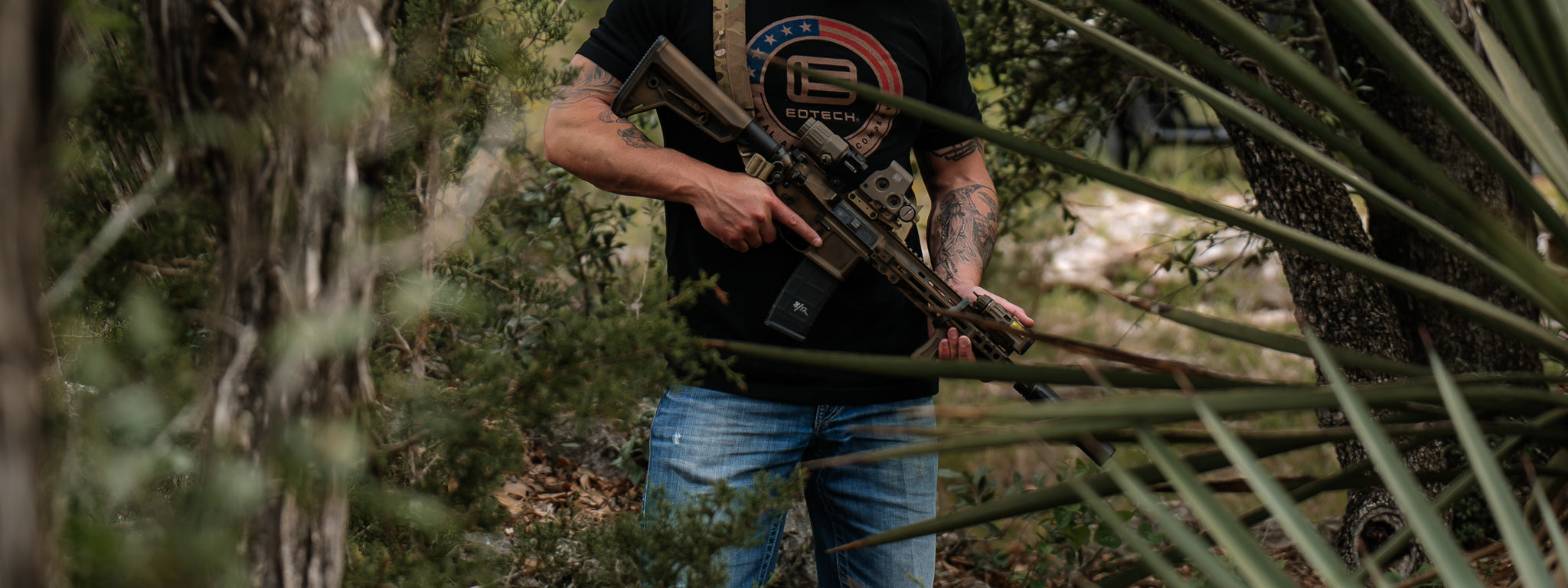 Man holding a rifle with EOTECH HWS optic and G33 magnifier in a forest setting