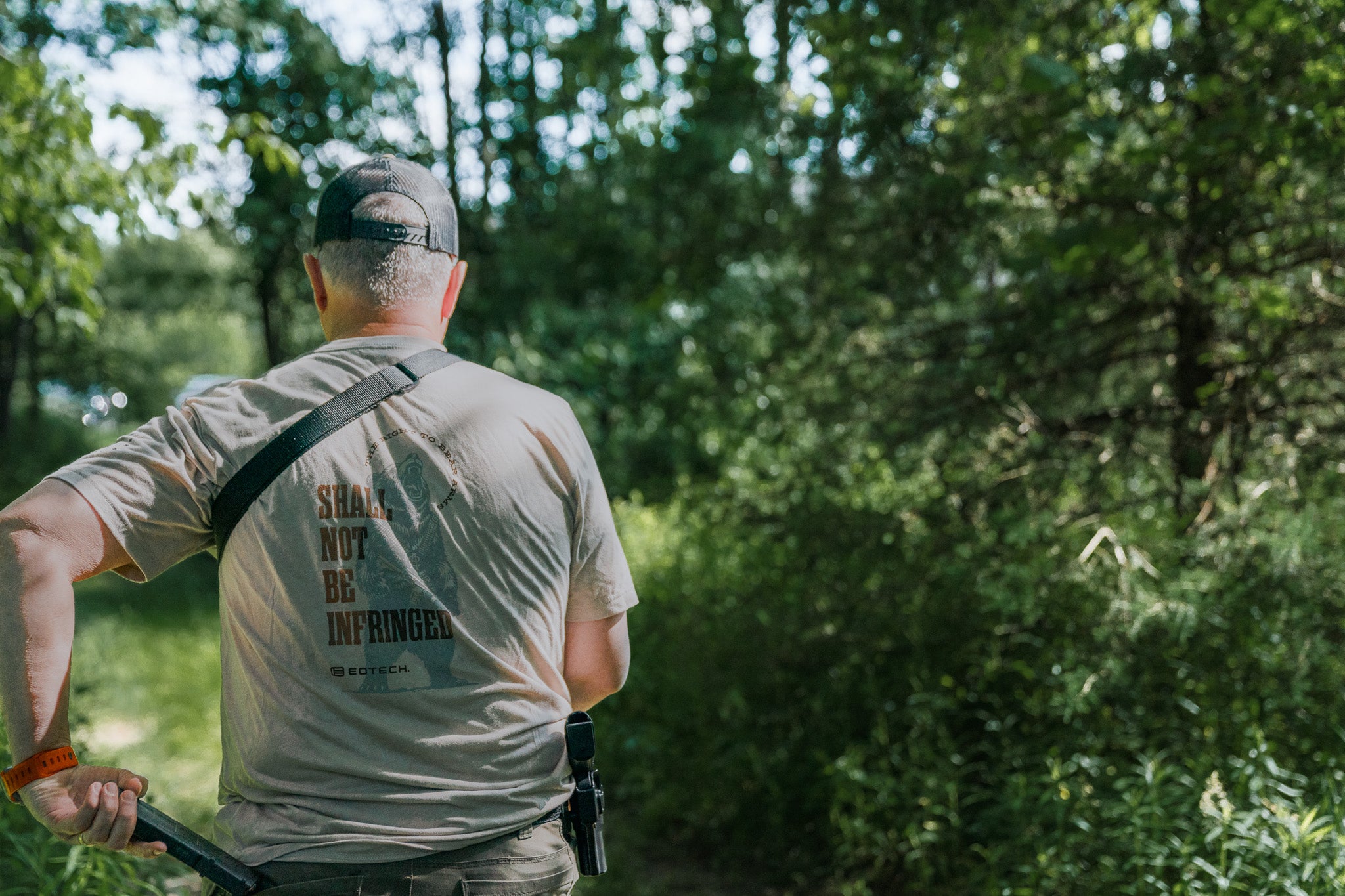 Person in a forest wearing a EOTECH Shall Not Be Infringed shirt, holding a rifle.