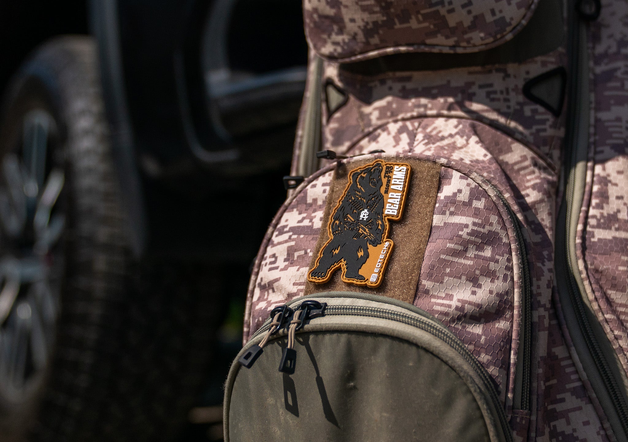 Camouflage backpack with a EOTECH Bear Arms patch on a blurred vehicle background