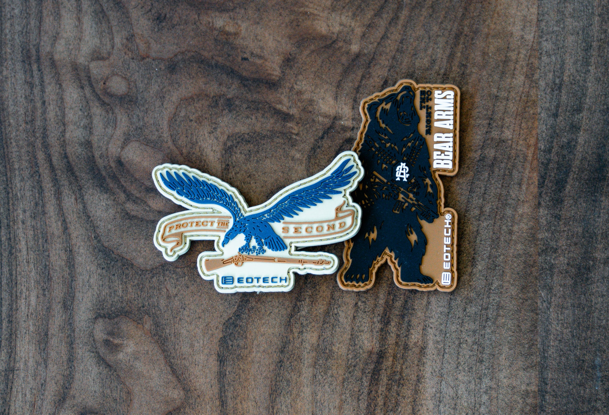 Two EOTECH logos patches on a wooden surface, one featuring an eagle and the other a bear.