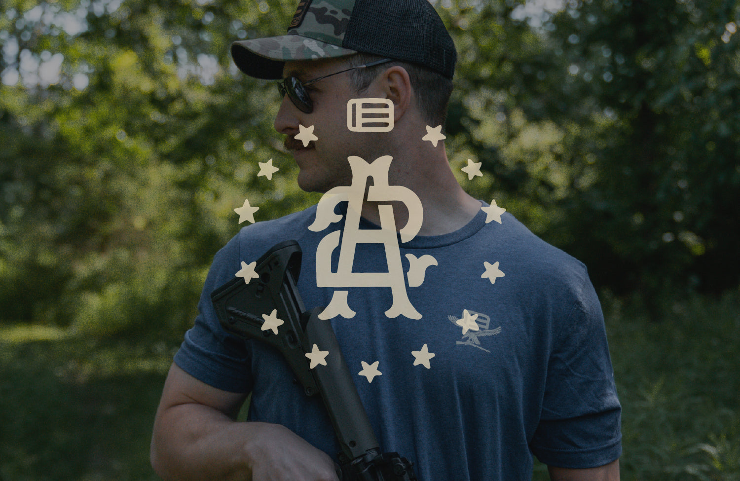 Man wearing a blue t-shirt with a 2A EOTECH logo, holding a rifle outdoors.
