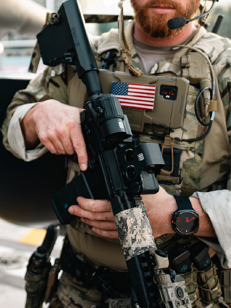 Person in military gear holding a black rifle with EOTECH HWS optic and magnifier and American flag patch