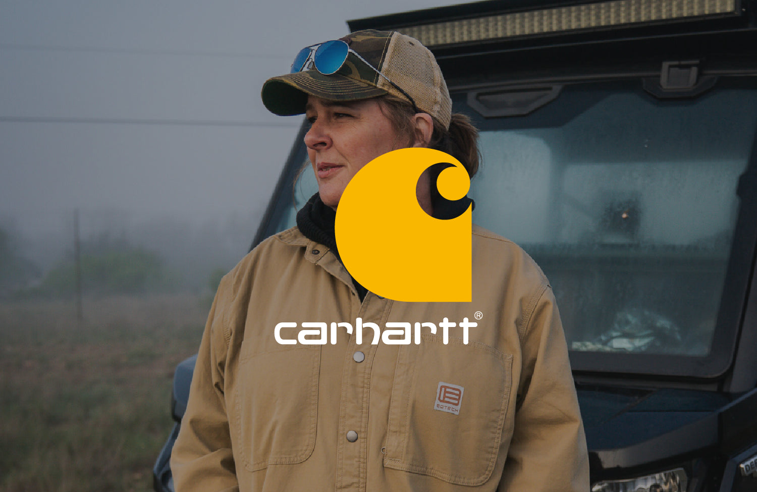 Woman wearing a Carhartt EOTECH jacket and cap standing next to a vehicle