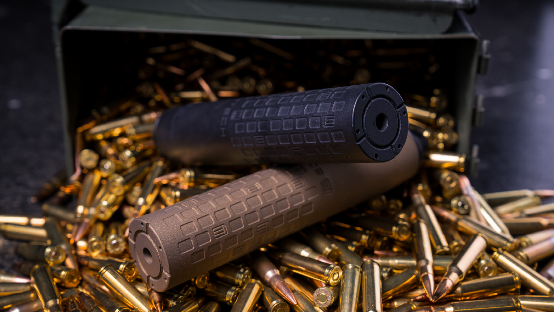 A black and a tan EOTECH DCBL suppressors on a bed of bullets with a dark background