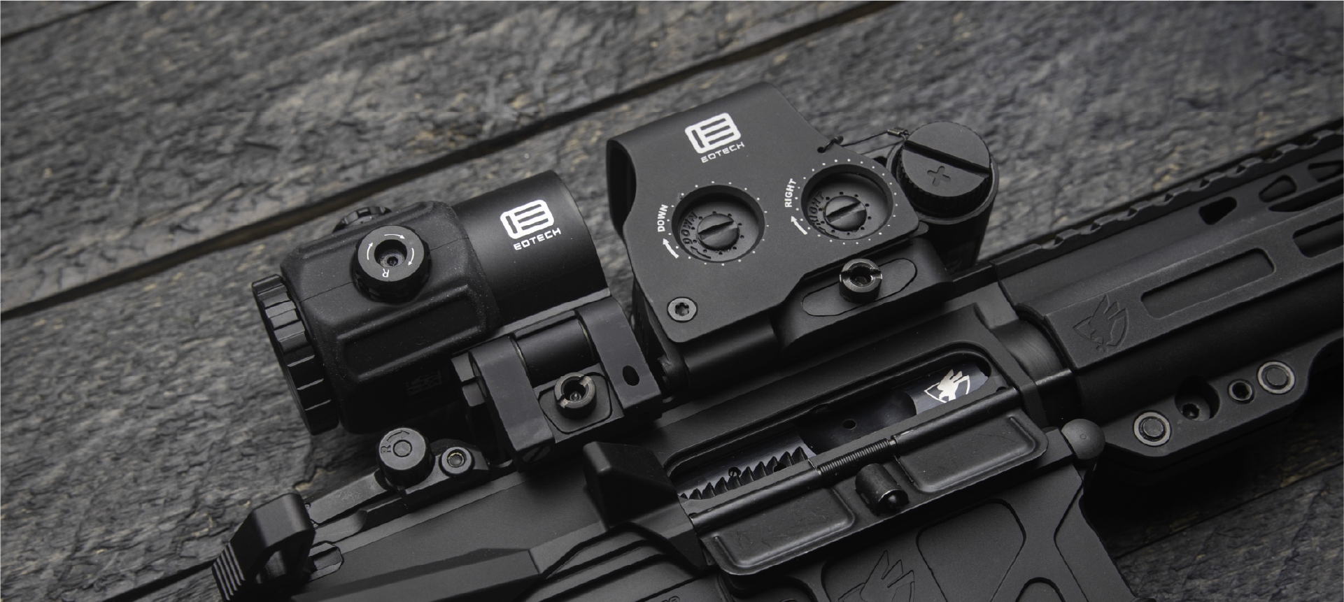 Close-up of a black rifle with EOTECH HWS optic and magnifier on a textured surface