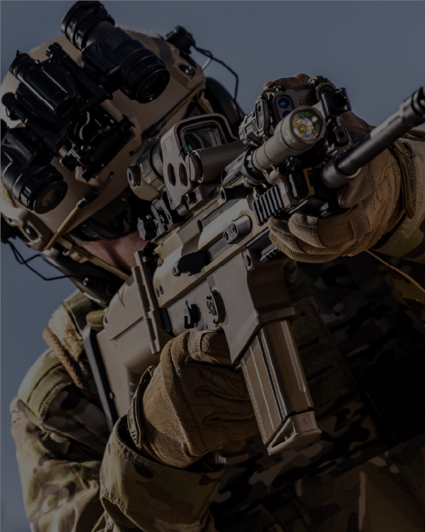 Person in tactical gear holding a tan rifle with a tan EOTECH HWS optic and OGL dark background