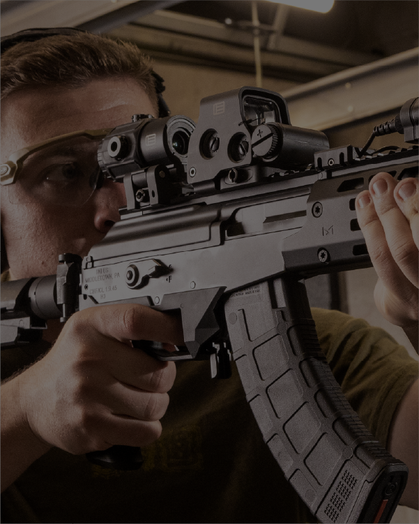 Person holding a rifle with a EOTECH HWS optic and magnifier in an indoor setting