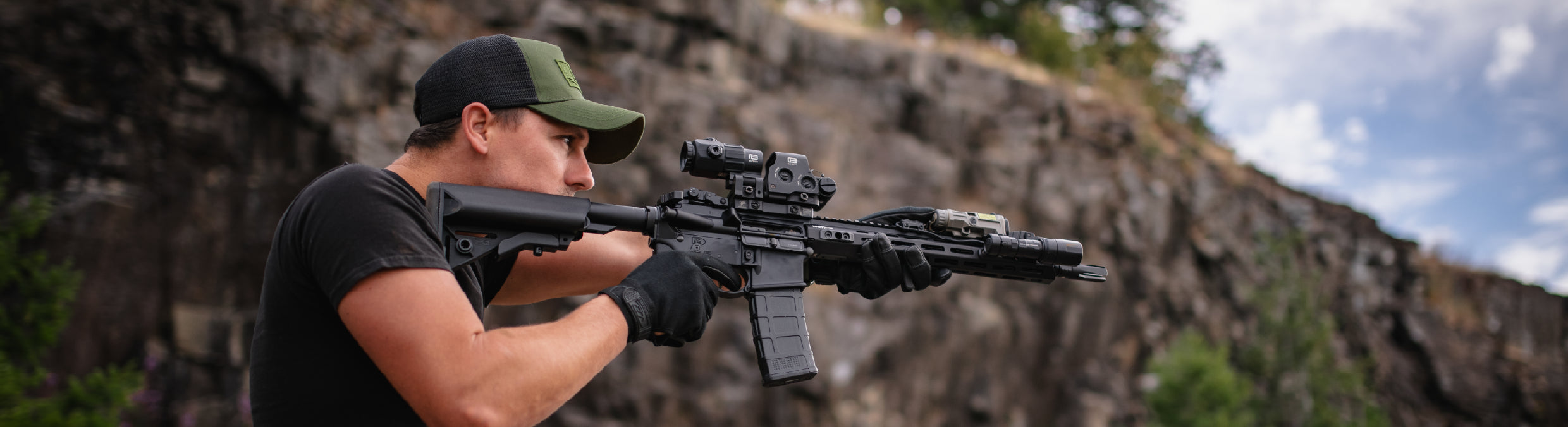 Person holding a rifle with a black EOTECH HWS optic and magnifier in a natural outdoor setting