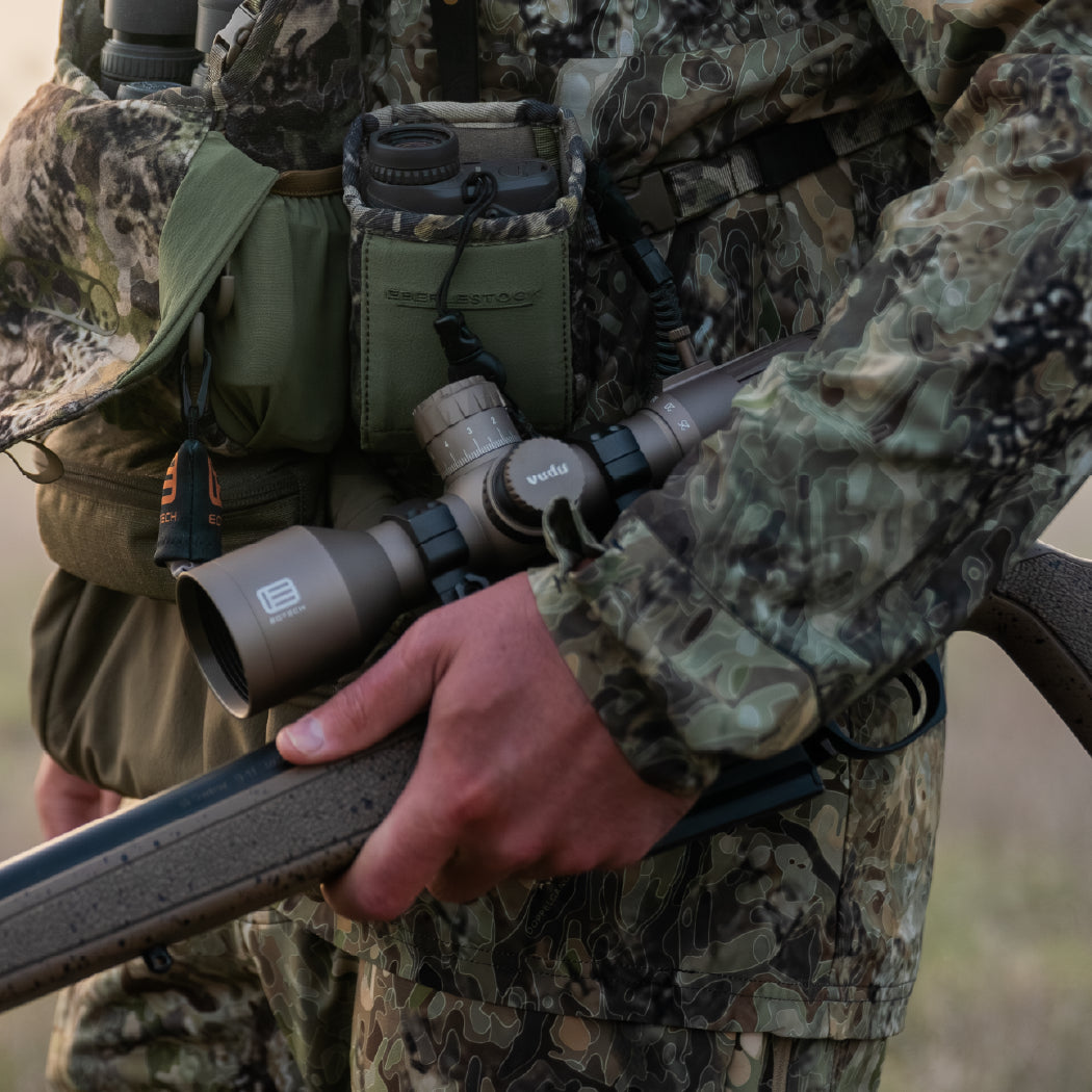 Person in camouflage holding a rifle with a tan EOTECH Vudu optic, likely in a hunting setting.