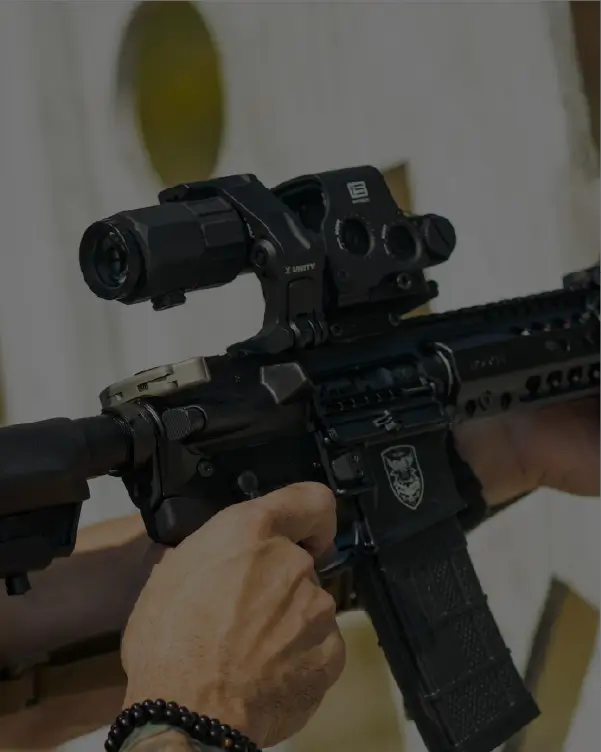 Close-up of a person holding an AR-15 rifle with a HHS Unity optic against a blurred background