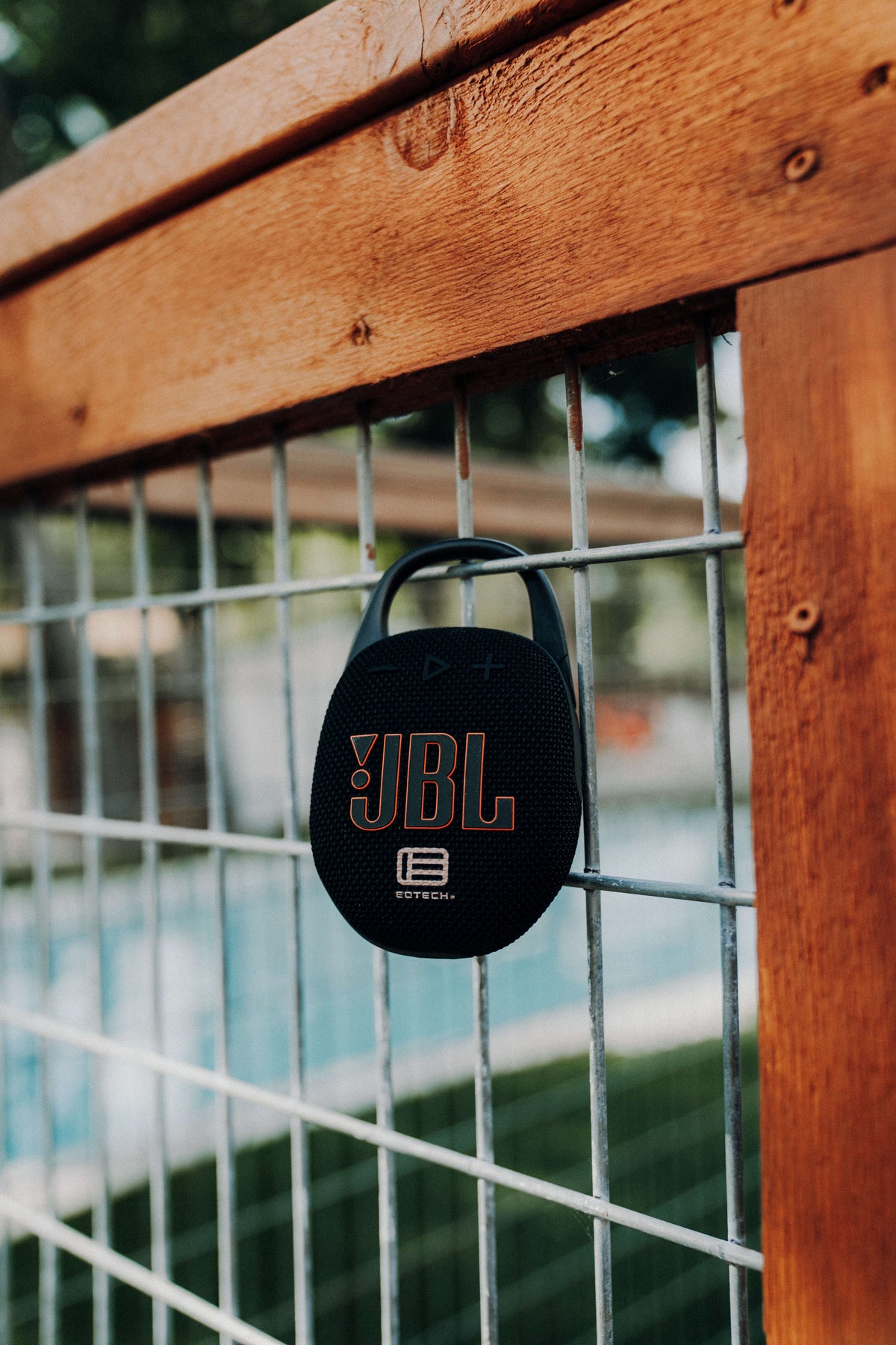 JBL Speaker clipped to a gate, a pool visible blurred in the background.