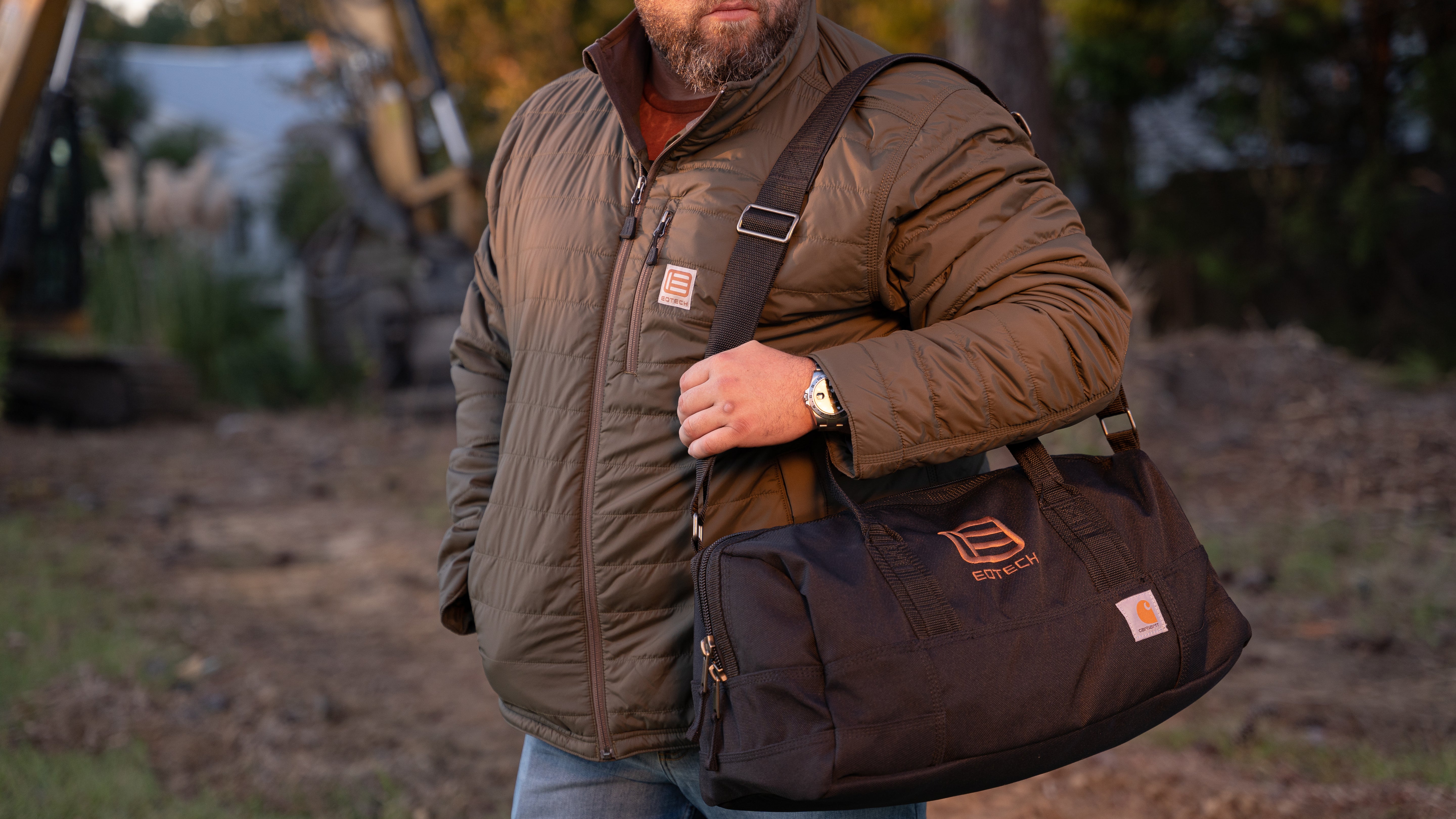Man holding a black EOTECH duffel bag with a blurred outdoor background