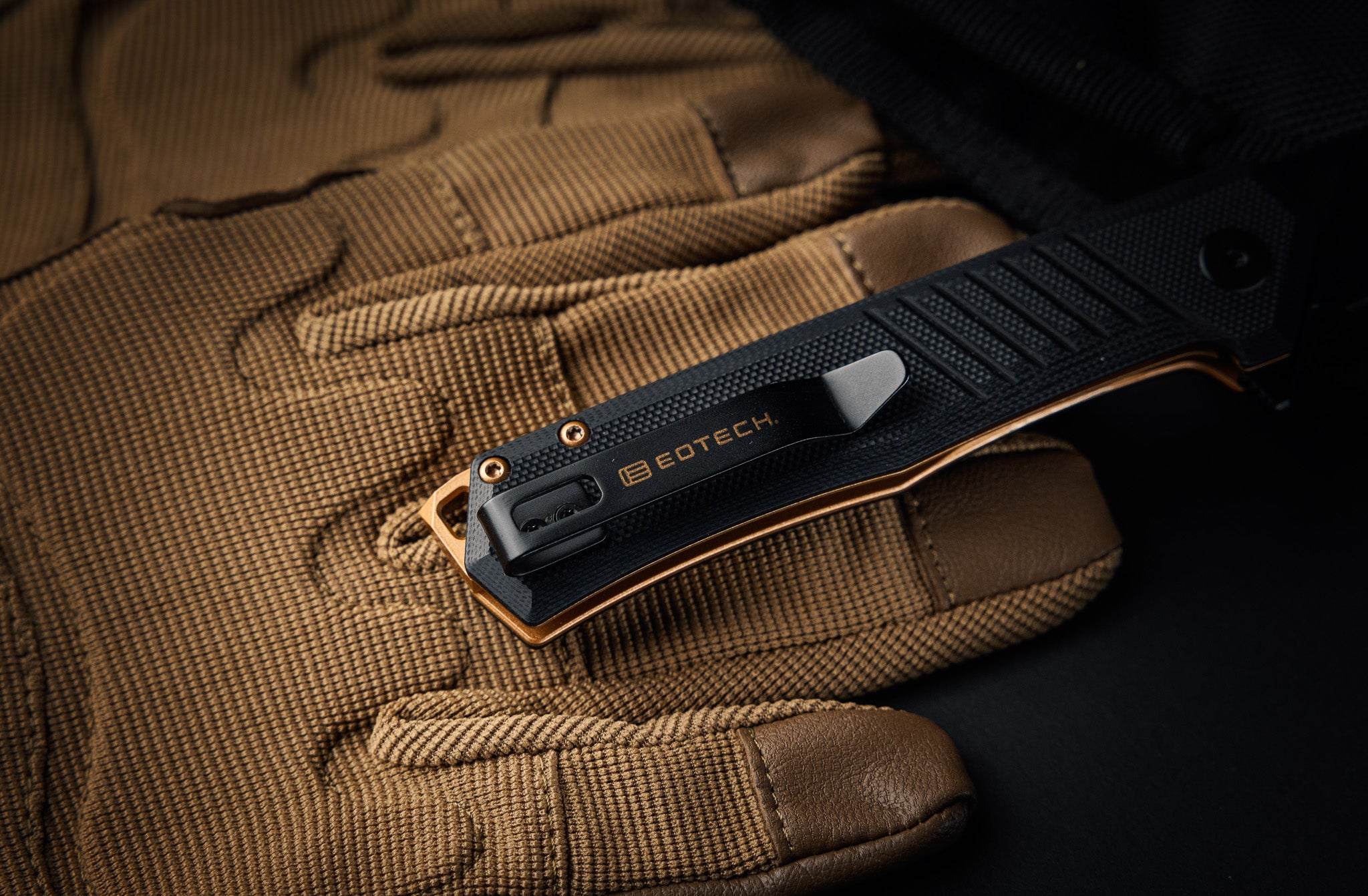 Black EOTECH knife on a brown tactical glove with a dark background