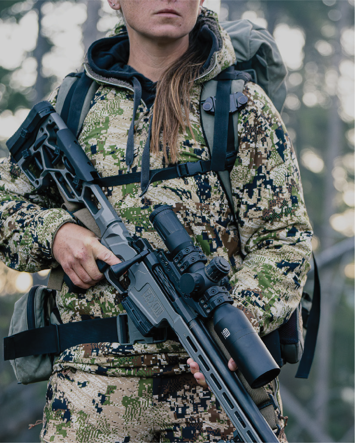 Female in camouflage gear holding a rifle with a EOTECH Vudu scope in a forest setting