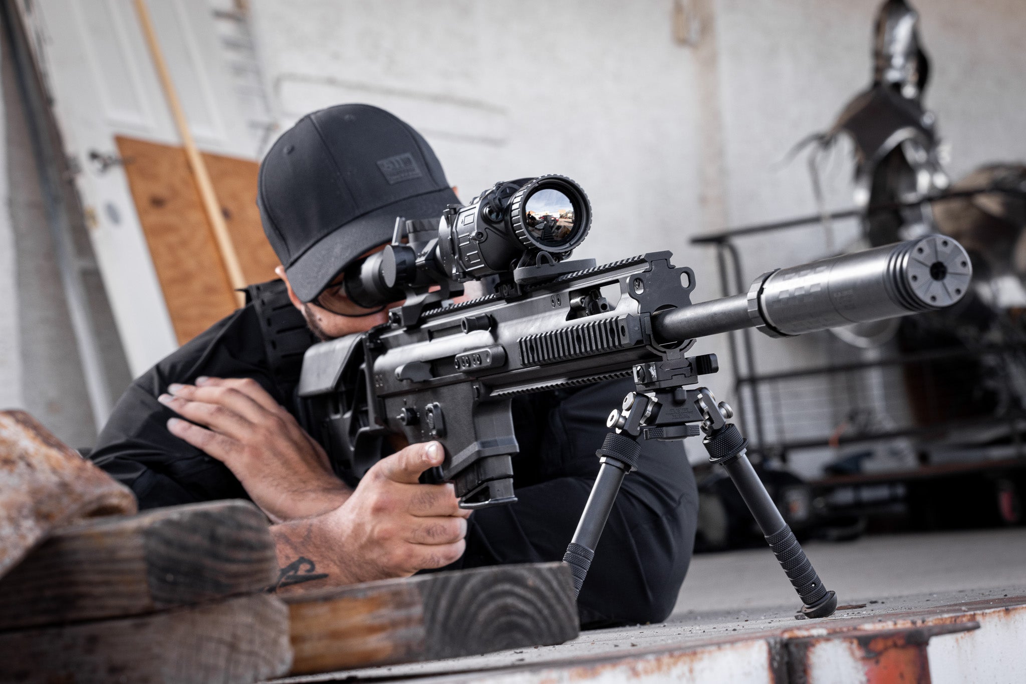 Man aiming a rifle with a EOTECH scope and DCBL suppressor  in an indoor setting