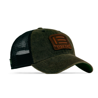 A trucker-style baseball cap with a washed olive green front panel and bill, black mesh back, and a brown rectangular patch on the front featuring a stylized 'E' logo and the word 'EOTECH'.