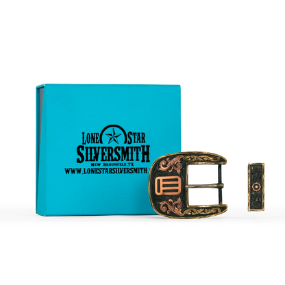 A decorative silver smith buckle with ornate filigree detailing, shown next to its turquoise branded presentation box on a white background.
