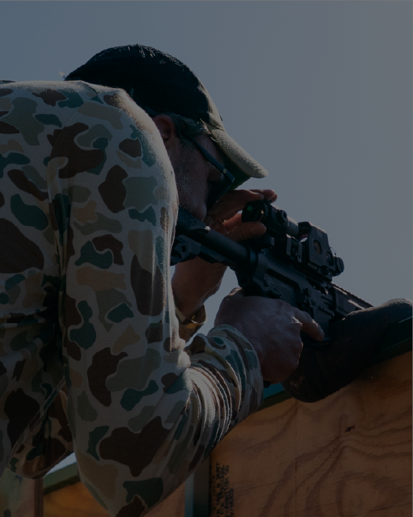Person in camouflage clothing aiming a rifle with black EOTECH HWS optic and magnifier a clear background