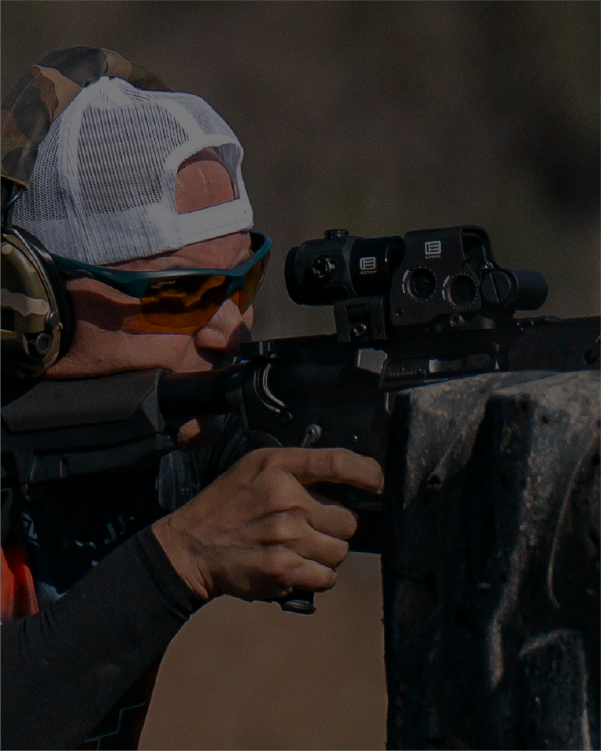Person in cap and glasses with a rifle black EOTECH HWS optic and magnifier, outdoor setting