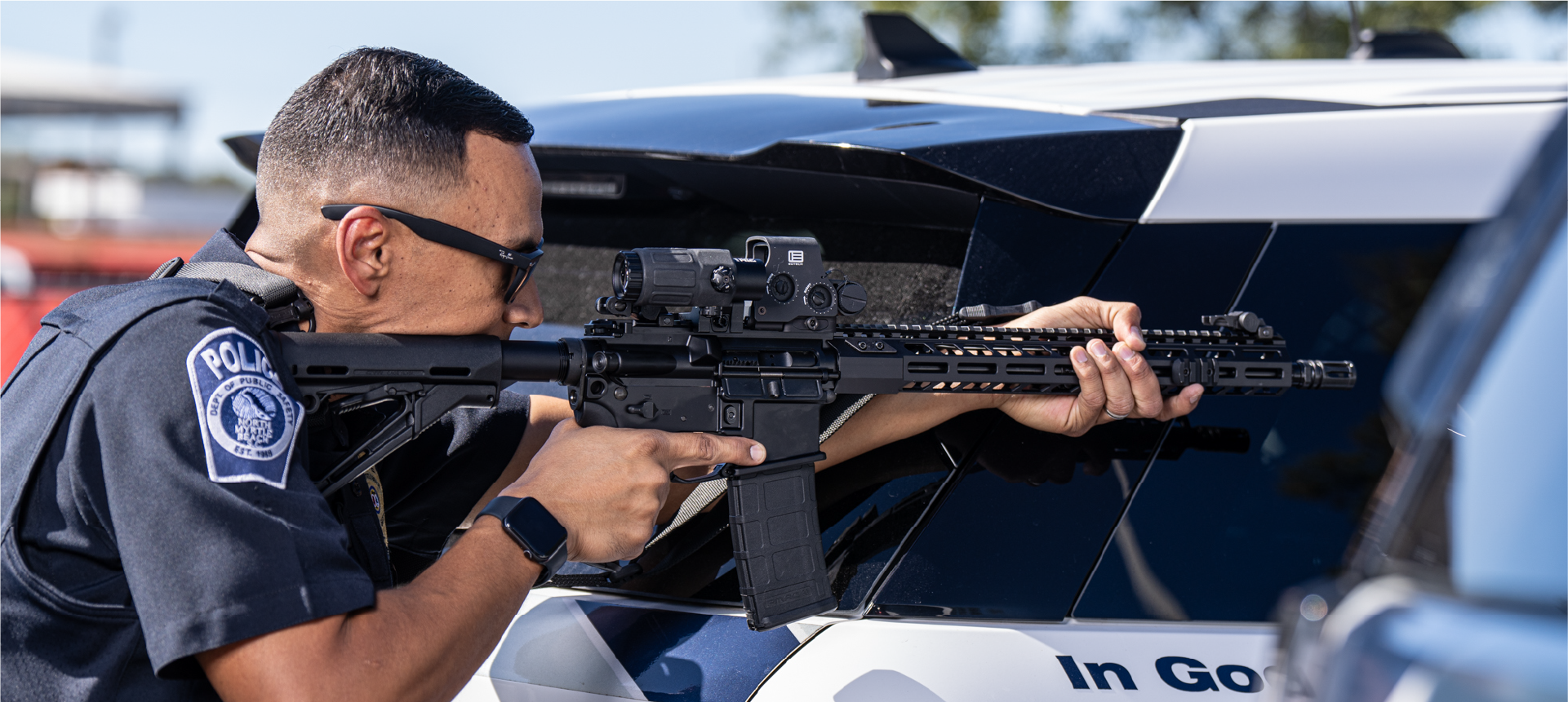 Police officer holding a rifle with black EOTECH HWS optic and magnifier in front of a vehicle