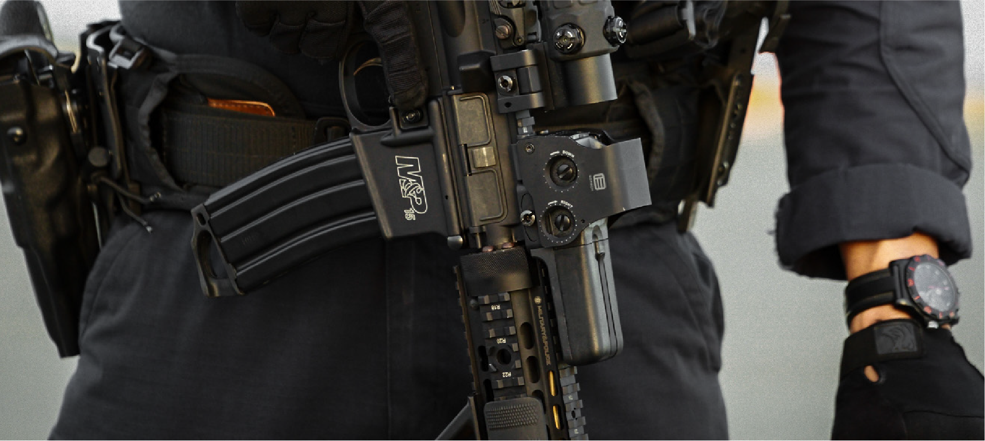 Person wearing tactical gear with a rifle and black EOTECH HWS optic and magnifier  blurred background