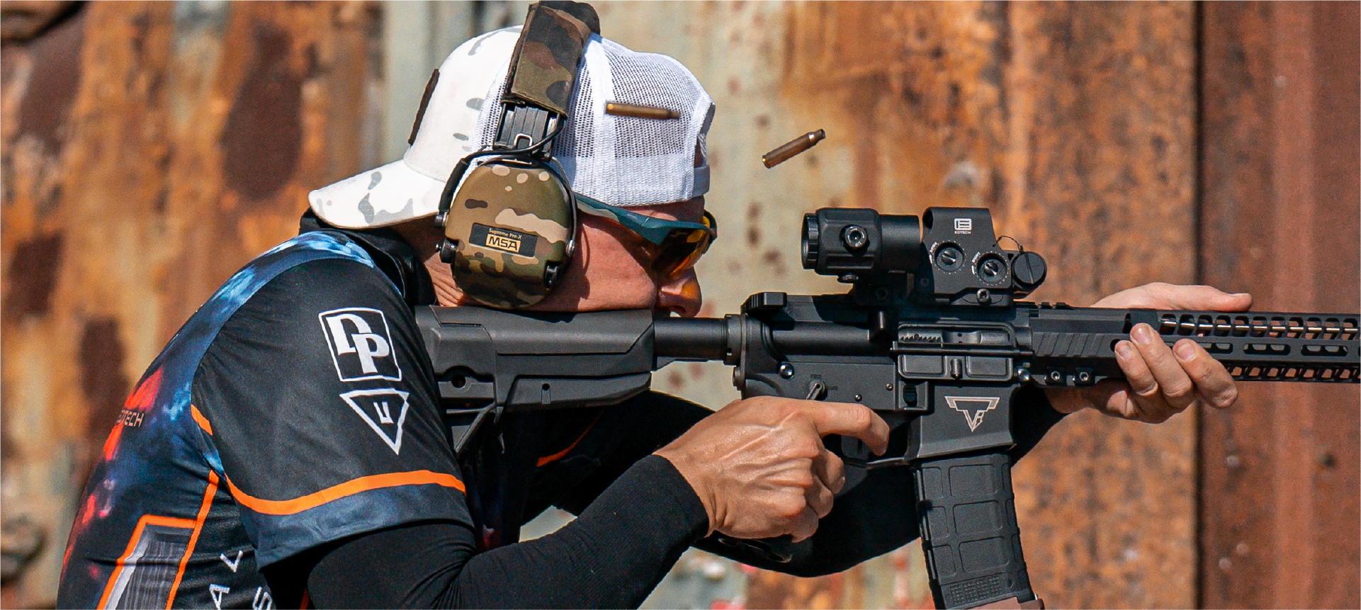 Person holding a rifle with a EOTECH HWS optic and magnifier against a rustic wooden background