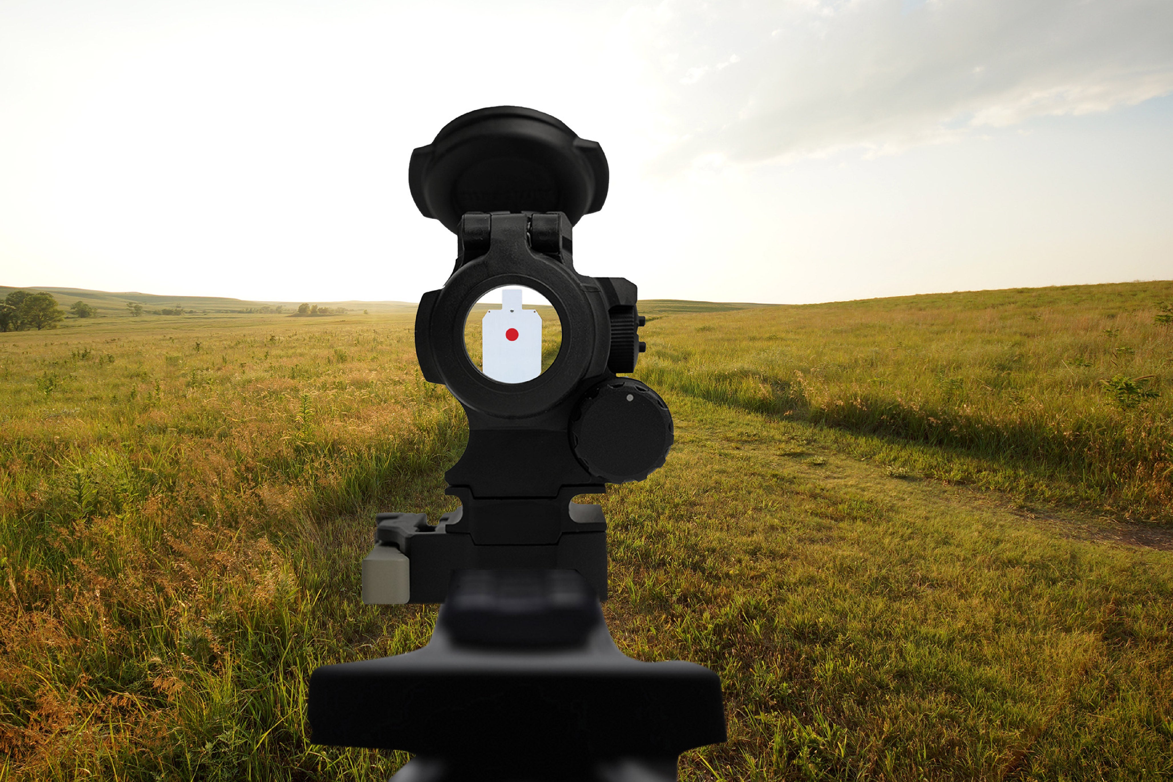 Red dot sight on a stand with a grassy field and cloudy sky in the background