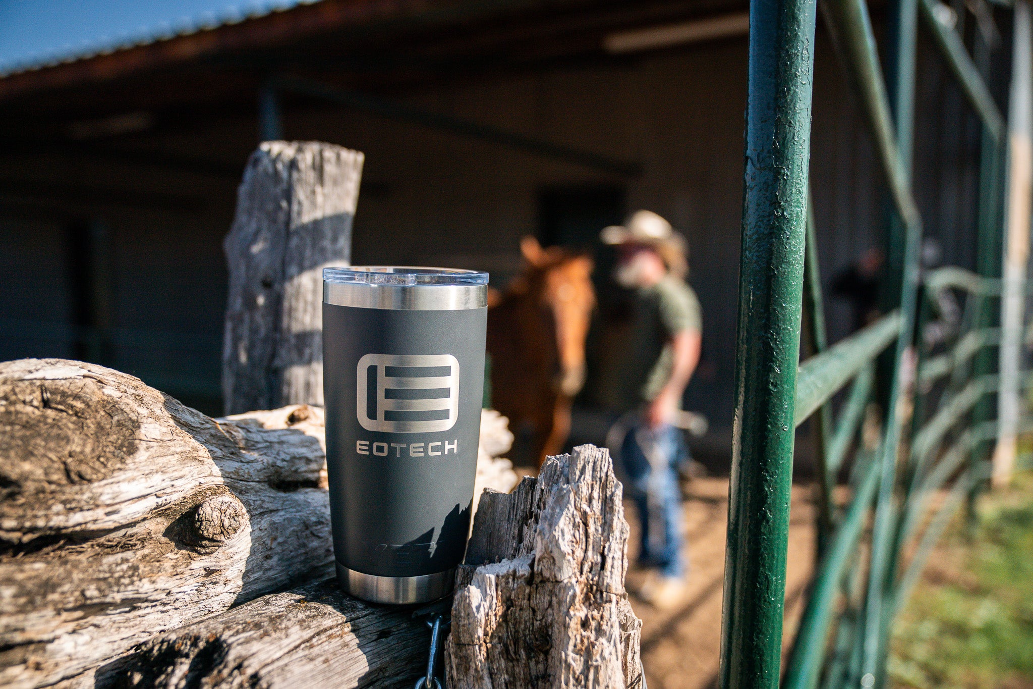 Eotech branded tumbler on a log with a person and horse in the background