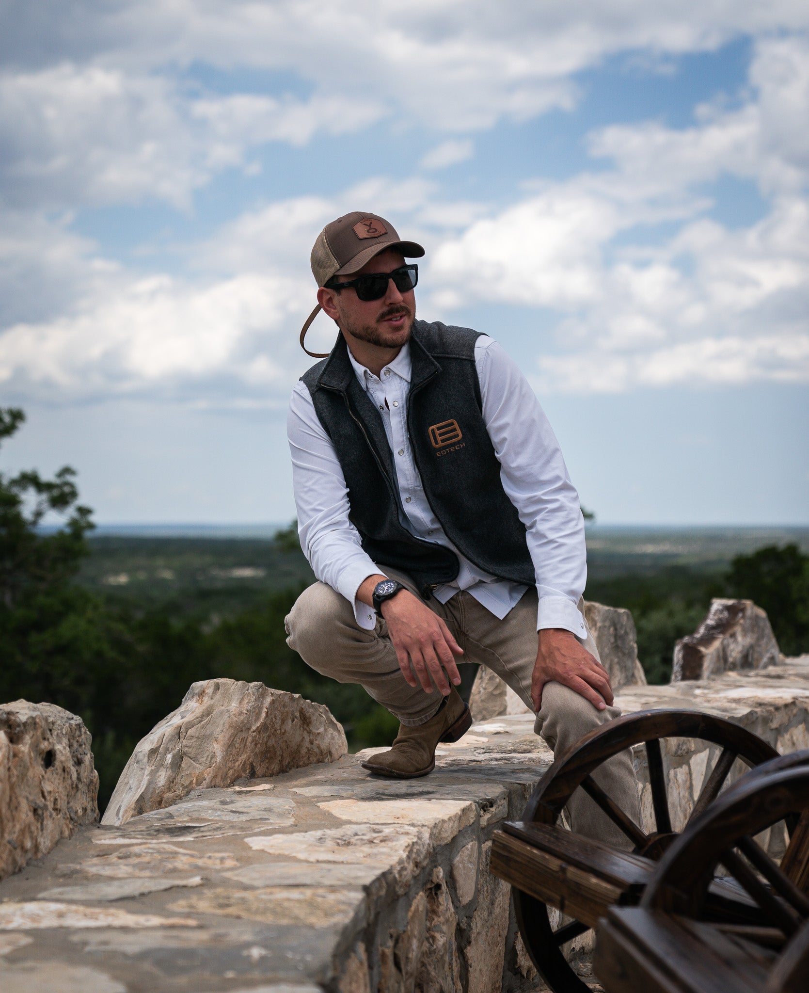 Man in EOTECH vest on stone steps with a scenic background