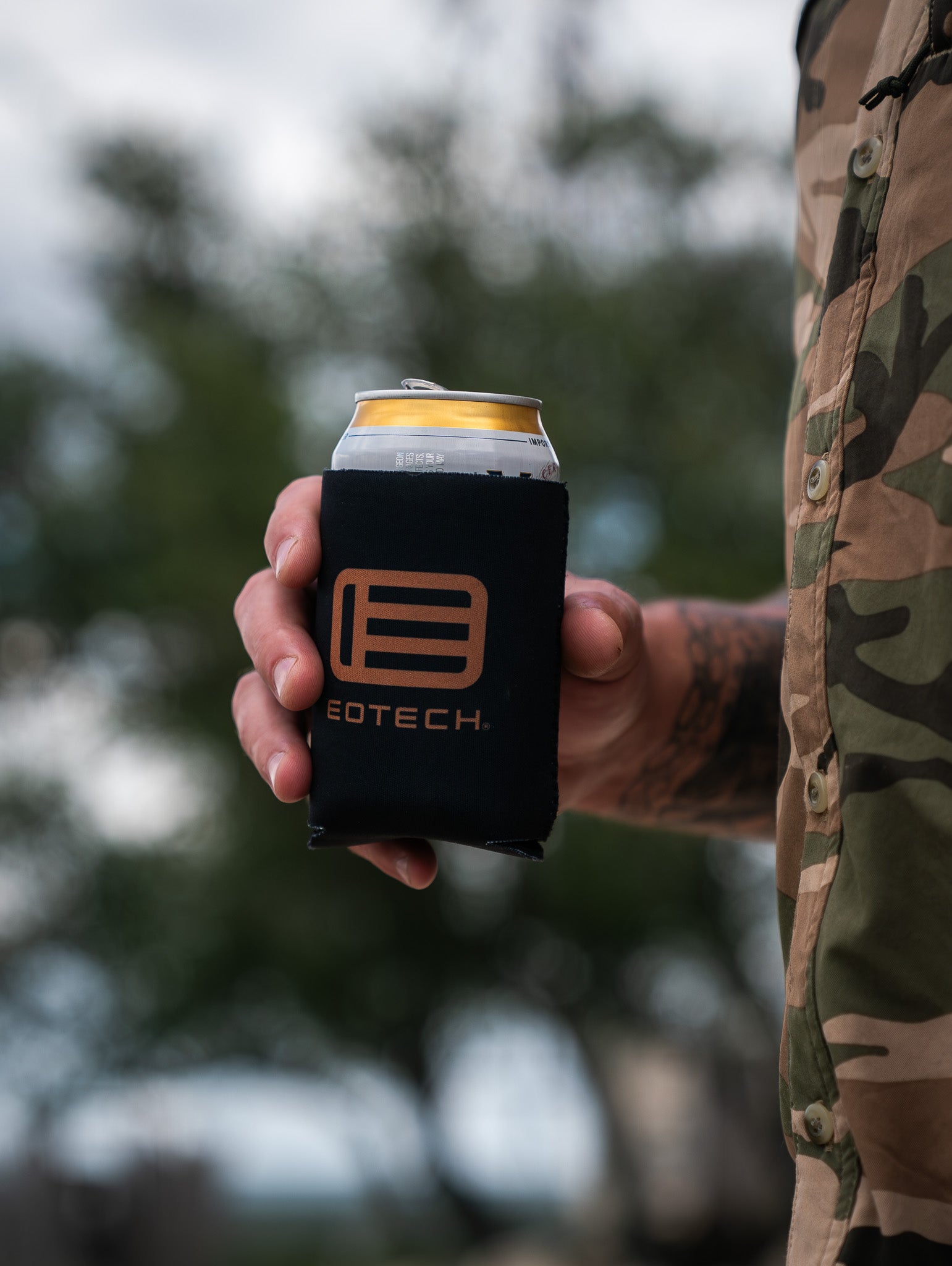 Person holding a can with EOTECH branding against a blurred natural background