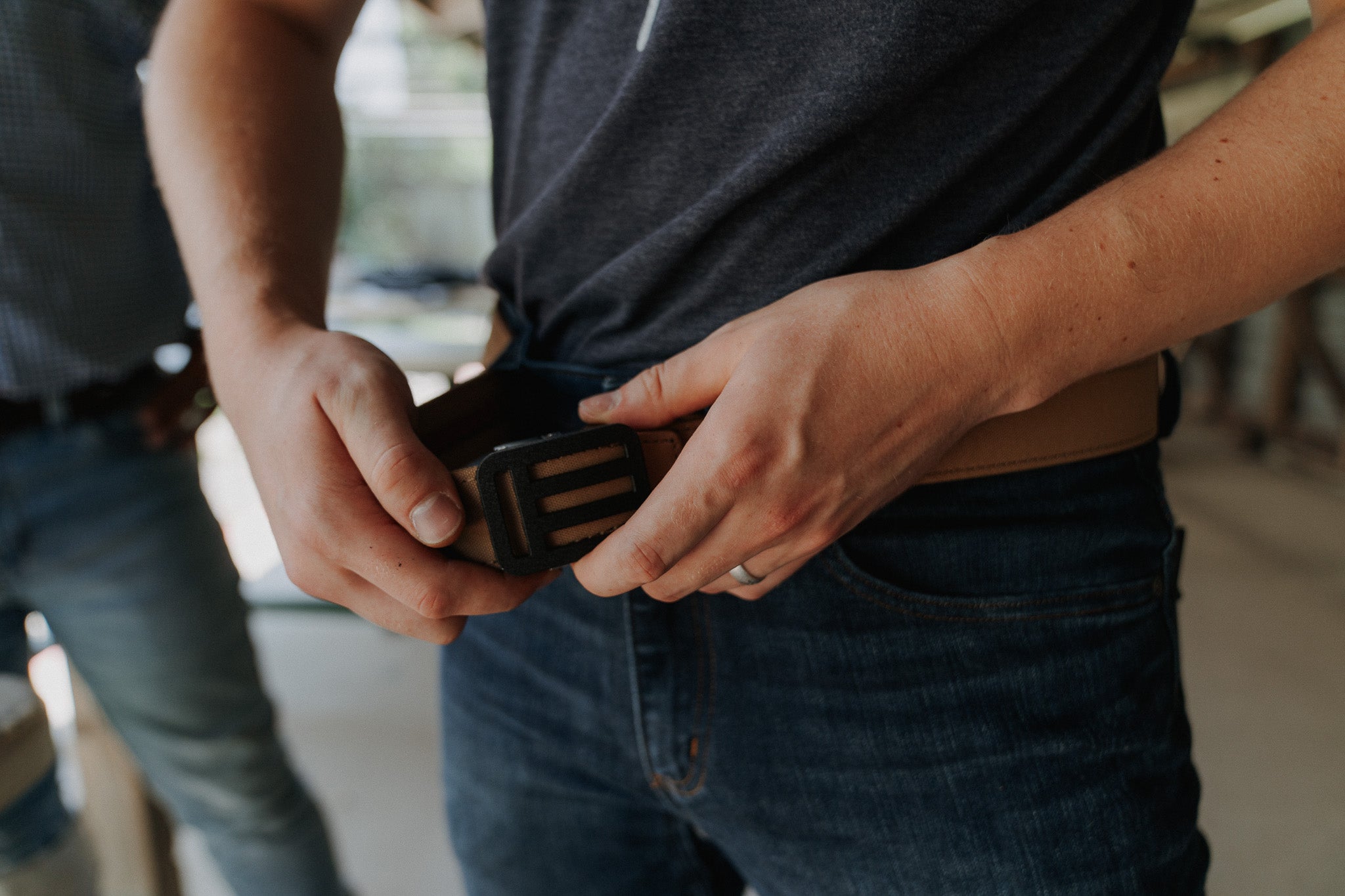 Person adjusting the tan EOTECH EDC belt with a blurred background