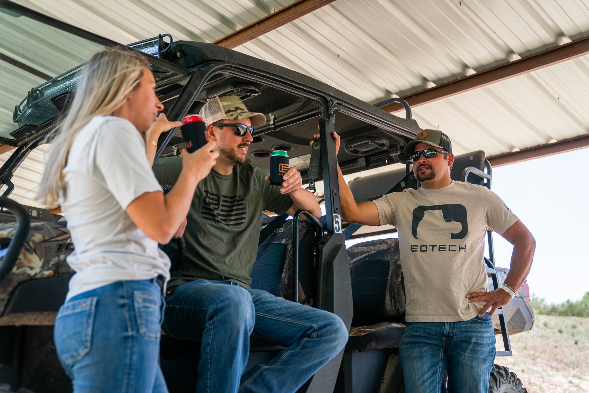 Three people interacting with a vehicle inside a building, one person wearing a EOTECH shirt.