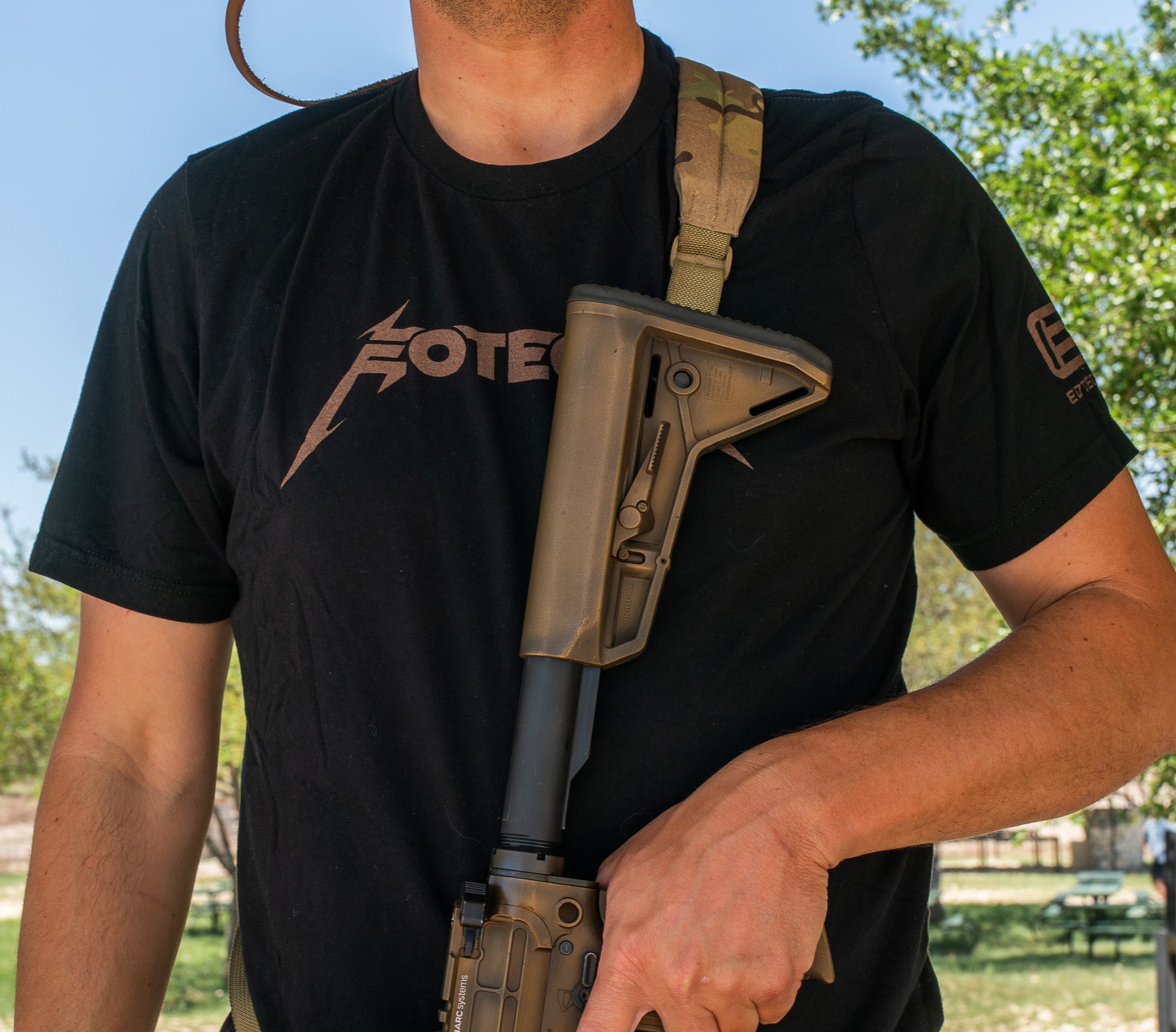 Person holding a rifle with a black t-shirt featuring a EOTECH logo in an outdoor setting