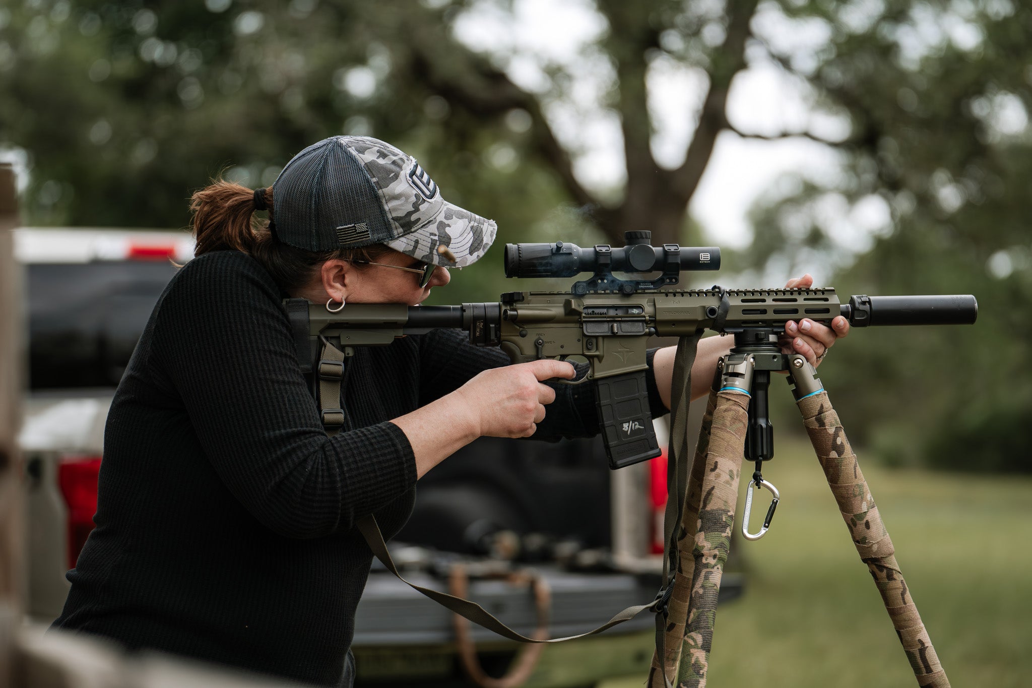 Woman aiming a rifle with a EOTECH Vudu scope on a tripod outdoors