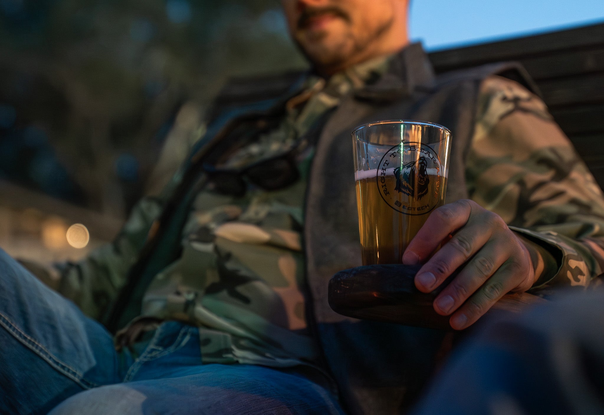 Man in camouflage jacket holding a EOTECH glass of beer outdoors