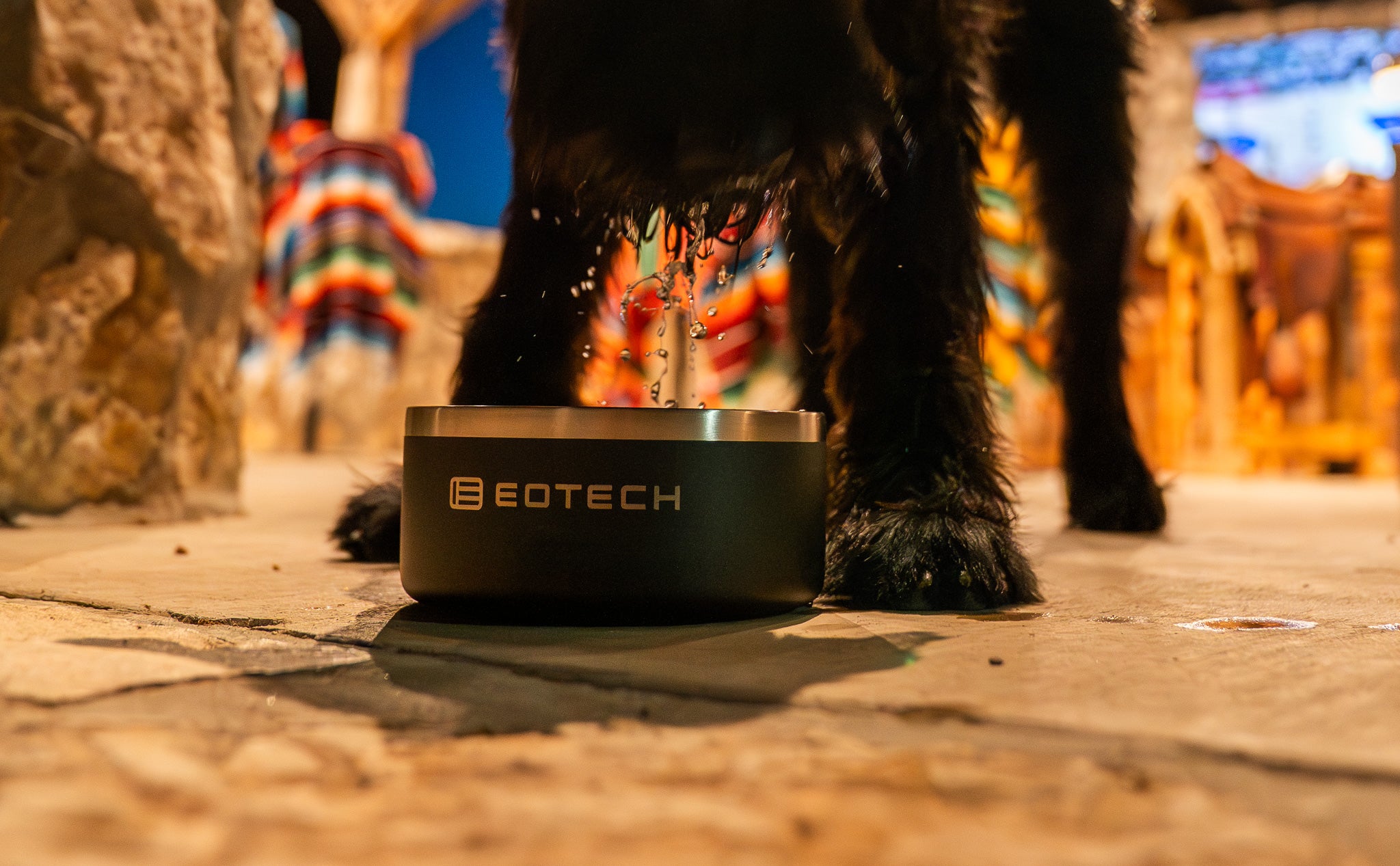 Dog drinking from a EOTECH branded water bowl on a stone surface.