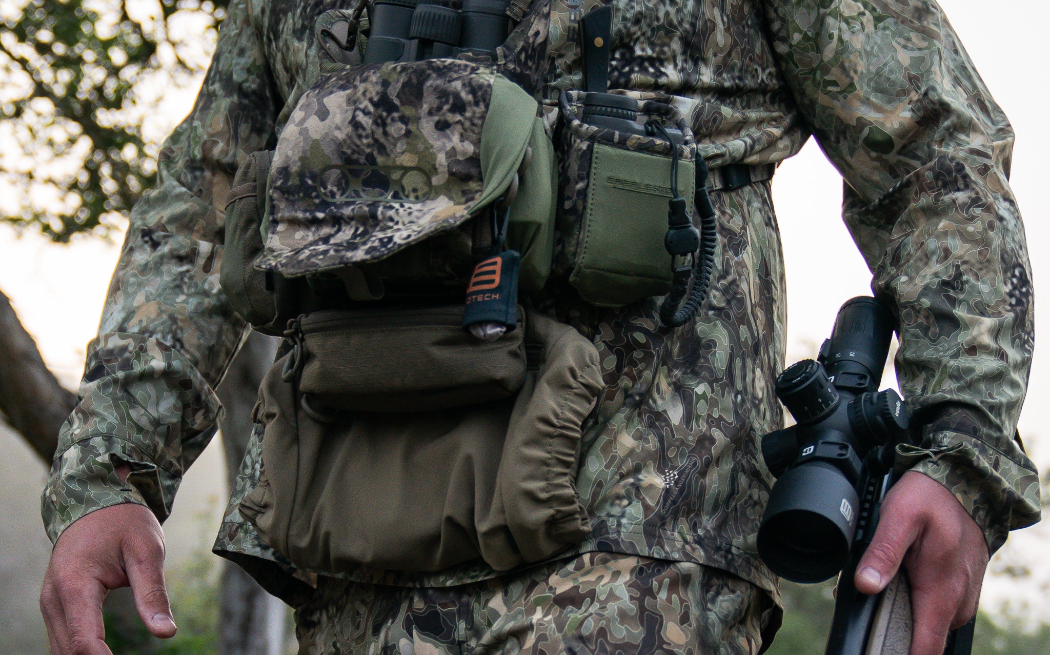 Person in camouflage gear holding rifle with VUDU optic outdoors
