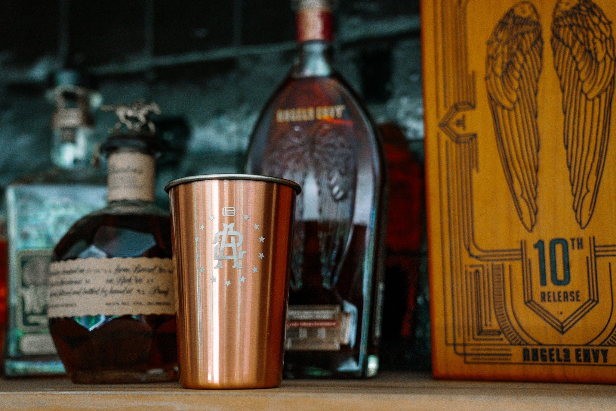 Bottle of whiskey with a EOTECH copper shaker and a box labeled '10th Release' on a wooden surface.