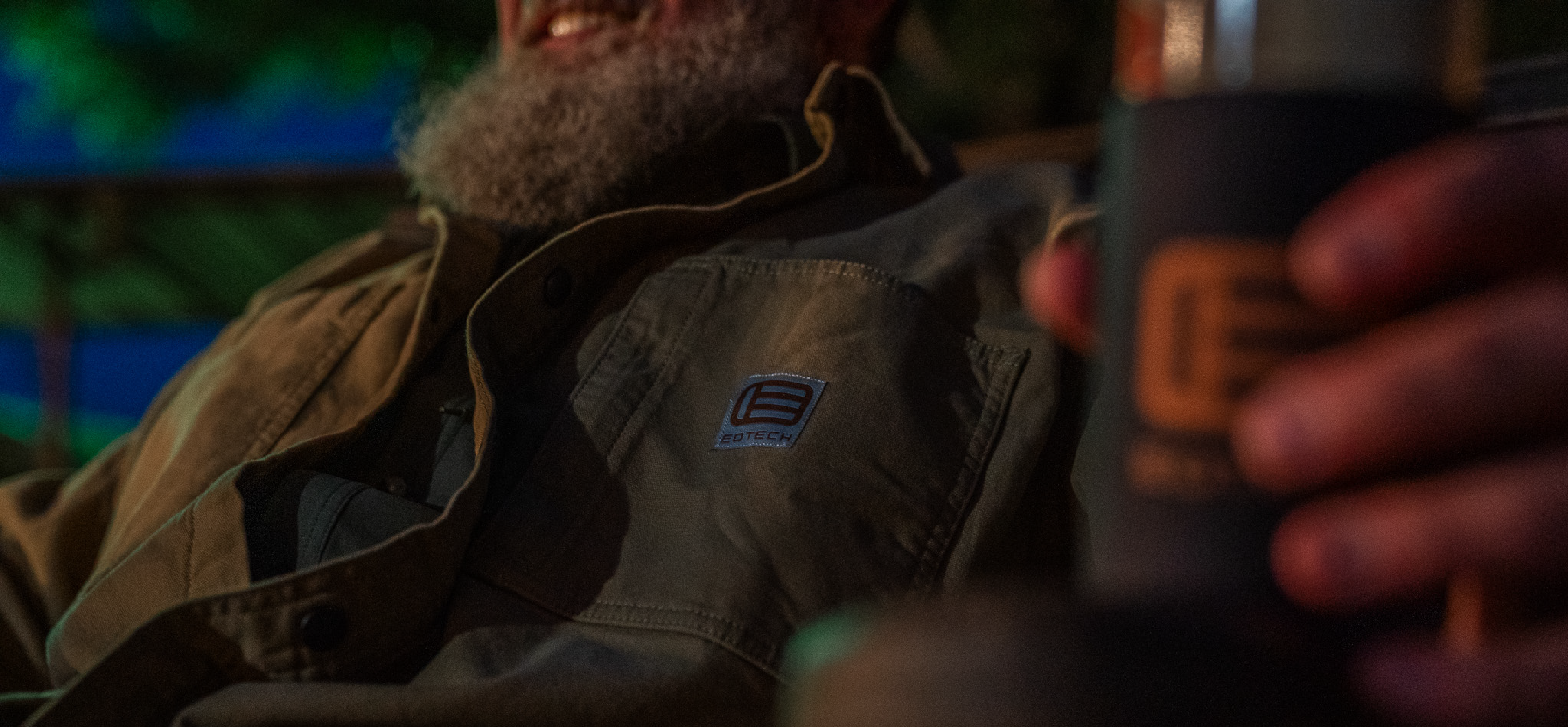 Man wearing a EOTECH jacket with a visible brand logo, holding a can.