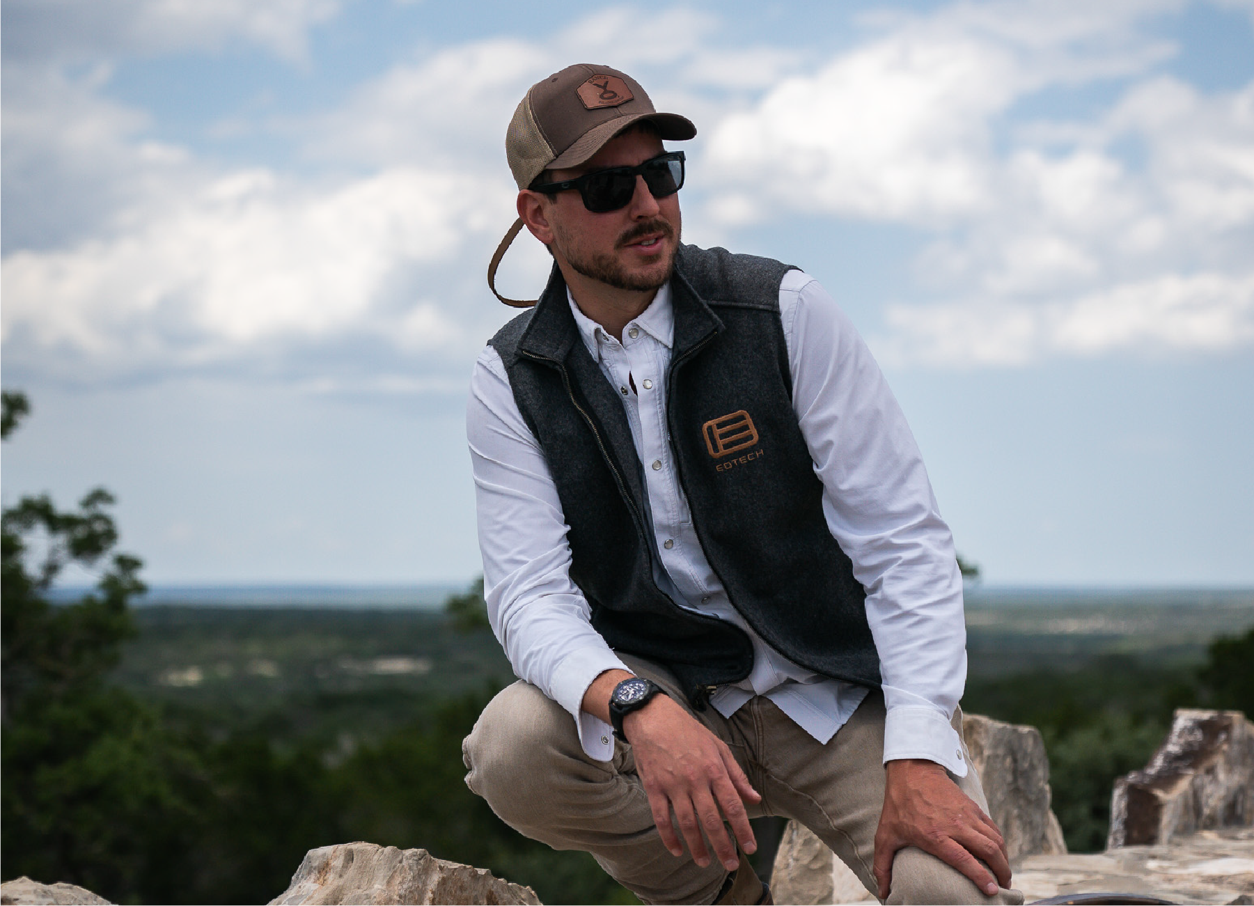 Man wearing a cap, sunglasses, and a EOTECH vest  outdoors