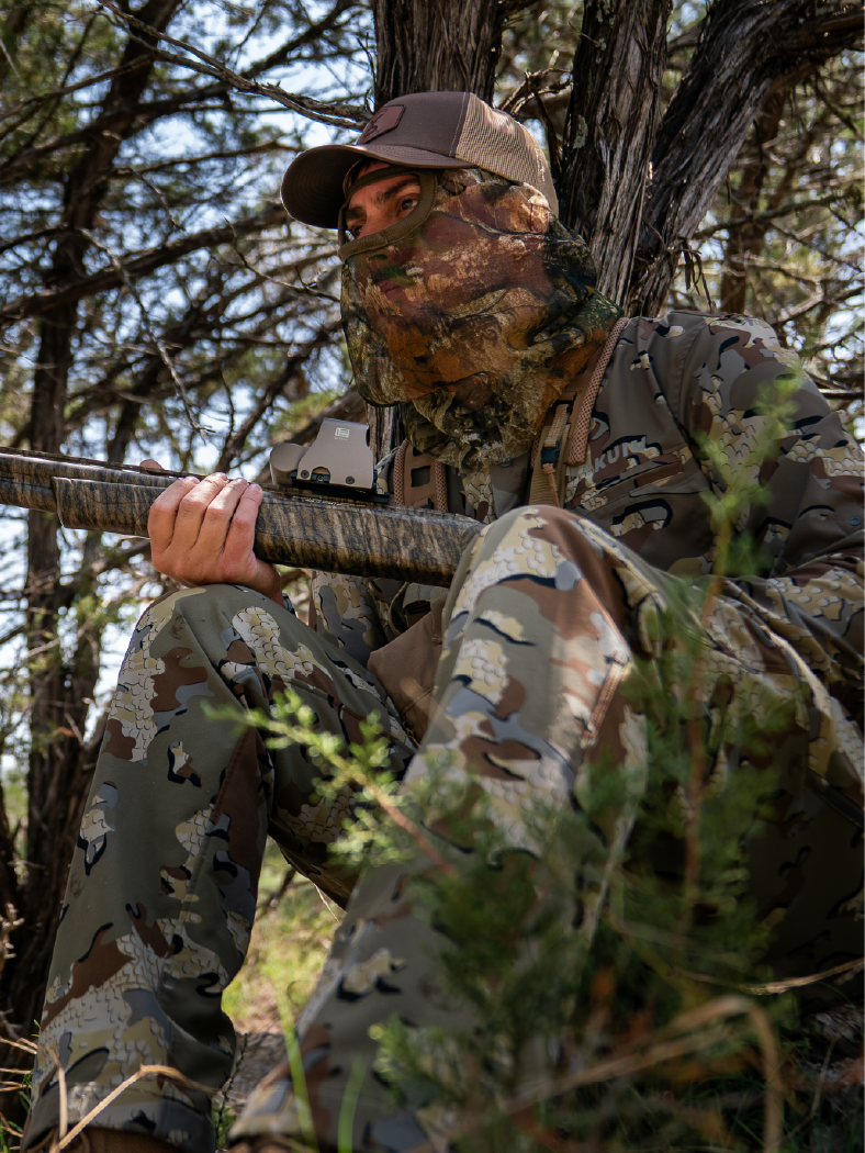Person in full camouflage gear holding rifle with EOTECH HWS optic in a forest setting