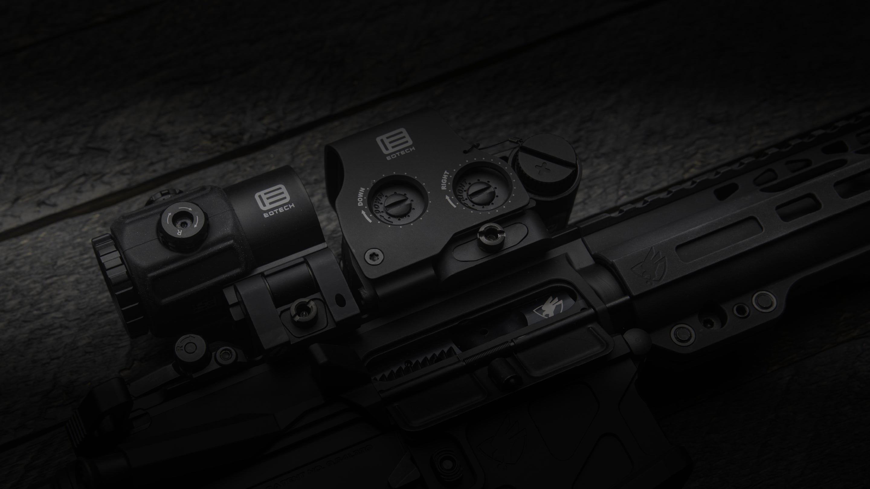 Close-up of a black rifle with EOTECH HWS optic and magnifier on a dark textured background